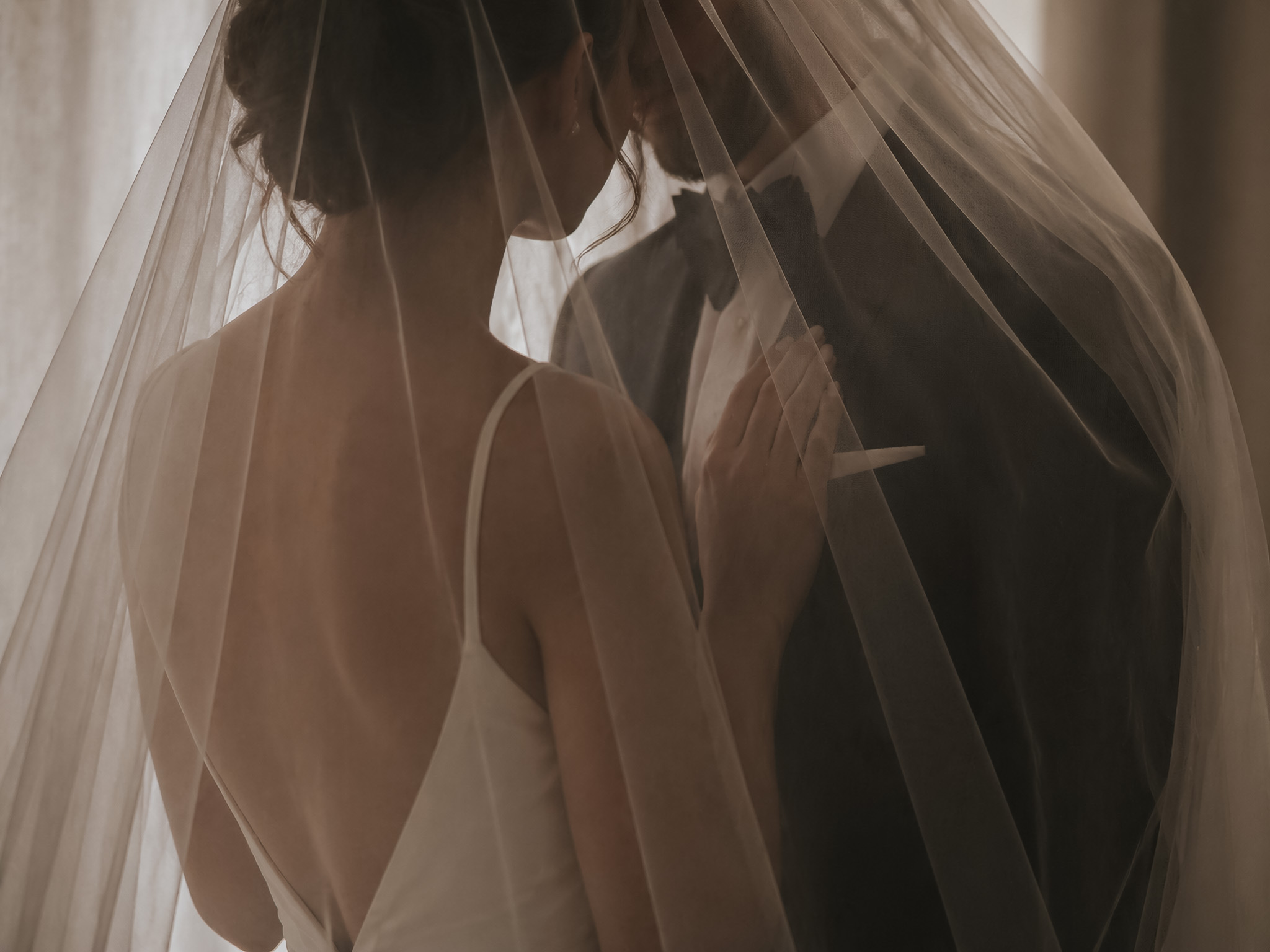 Bride and partner partially hidden beneath a veil in a private wedding moment