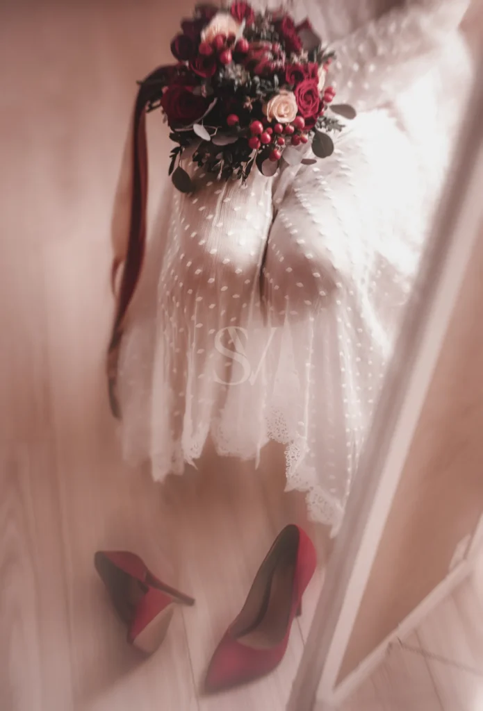 Red bridal heels and bouquet behind sheer wedding fabric