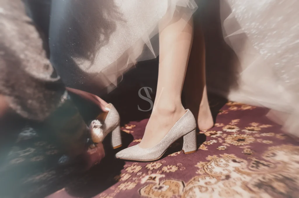 Hands helping a bride put on a silver wedding shoe