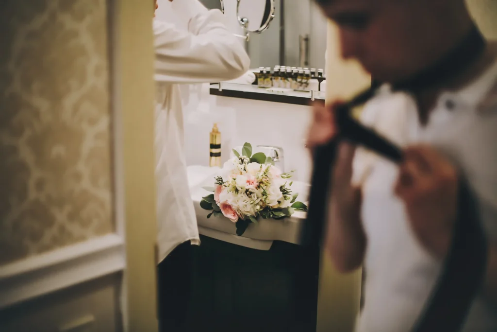 Groom adjusting his bow tie beside a wedding bouquet
